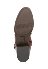 Sole di stivale in pelle marrone con superficie testurizzata e scanalature orizzontali. Presenta una forma rotonda e un logo in rilievo sulla suola.