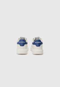 Tênis brancos com um detalhe azul no calcanhar. Parte superior em pele lisa, biqueira arredondada e sola texturizada. Logótipo impresso no calcanhar.