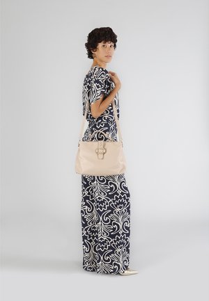 Beige læderhåndtaske med flettet detalje, justerbar rem og sølvhardware, parret med et navy- og hvidmønstret outfit.