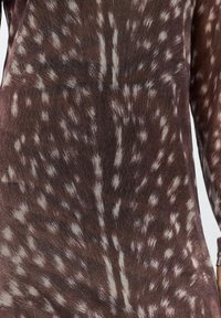 Brązowy i biały materiał w stylu tie-dye z długimi rękawami, ukazujący zbliżenie teksturowanego wzoru odzieży oraz subtelnych zmarszczek.