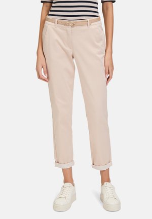 Beige trousers with a tailored fit, cuffed hems, side pockets, and a matching belt featuring a circular buckle. Worn with white sneakers.