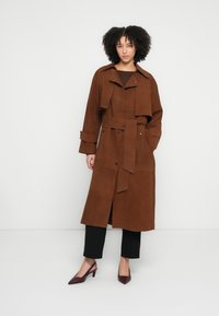 Barna színű, velúr anyagú ballonkabát övvel a deréknál, széles hajtókákkal és gombdíszítéssel. Fekete nadrággal és bordó magassarkú cipővel párosítva.