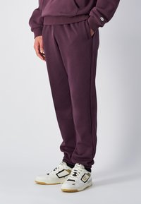 Verbrande paarse joggingbroek met een relaxte pasvorm, elastische tailleband en zijzakken, gecombineerd met wit-gouden sportschoenen.