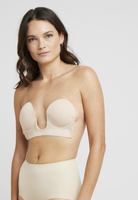Nude strapless bra with a plunging neckline, molded cups, and seamless edges. Designed for a smooth fit against the skin.