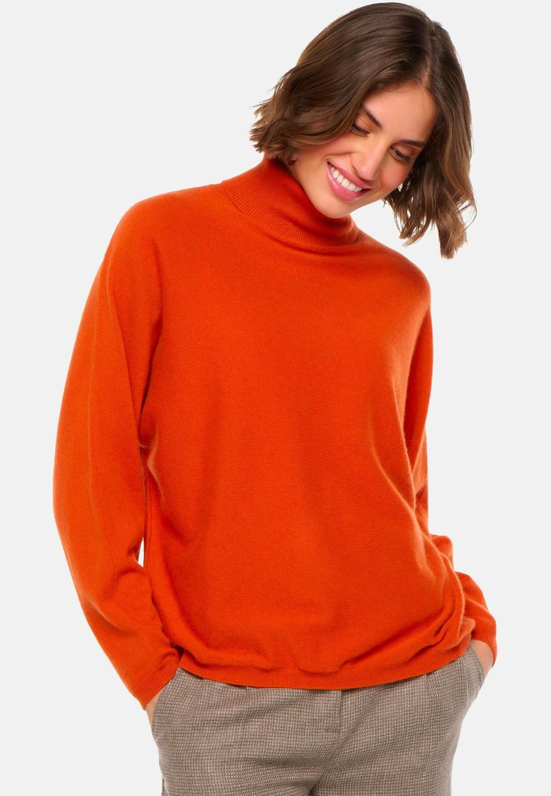 Pull léger orange en col roulé, fabriqué dans un tissu doux, avec une coupe décontractée et des manches longues, associé à un pantalon à motifs.