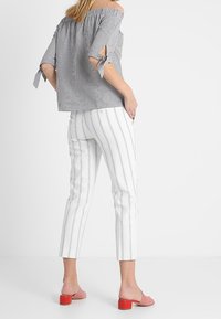 Randig off-shoulder topp i grått och vitt, ihop med vita byxor med vertikala ränder. Rosa blockklackade slides fulländar looken.