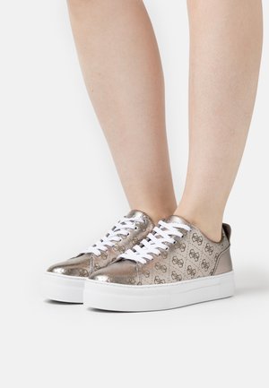 Sneakers metallici argentati con lacci bianchi, caratterizzati da un motivo a logo ripetuto sulla tomaia e una spessa suola in gomma bianca.