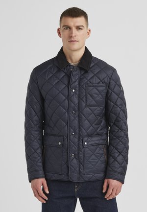 Navy quilted jacket with a corduroy collar, snap front closure, and two zippered side pockets. Features a chest pocket and textured pattern.