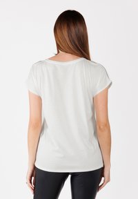 Camiseta de manga corta gris claro con cuello redondo y puños enrollados, que presenta un corte relajado y una textura suave. Se llevan leggings negros.