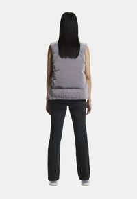 Grå dunvest med høj krave, ærmeløst design, vertikal quiltet tekstur og en let oversized pasform, parret med sorte stribede bukser.