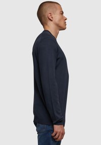 Navy sweatshirt med lange ermer, ribbestrikkede mansjetter og rund halslinning. Myk tekstil med en glatt overflate, vist på en modell i profil.