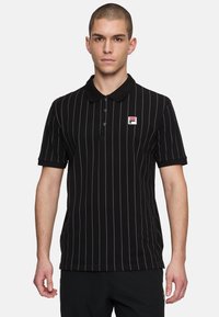 Svart polo t-shirt med tunna, vertikala vita ränder, kortärmad och med krage. Har en liten broderad logotyp på vänster bröst.