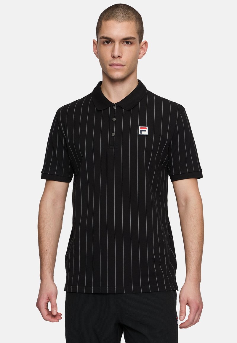 Svart polo t-shirt med tunna, vertikala vita ränder, kortärmad och med krage. Har en liten broderad logotyp på vänster bröst.