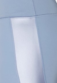 Vaaleansiniset leggingsit, joissa on sileä kangaspinta; varustettu kontrastivärisellä vaaleammalla sivupaneelilla, kirjotut saumat ja istuva malli.