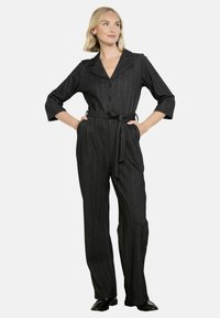 Musta viivapuku, jossa on huppukaulus, kolmanneksen hihat, etunapit ja sidottava vyö. Leveä lahje ja teksturoitu kangas.