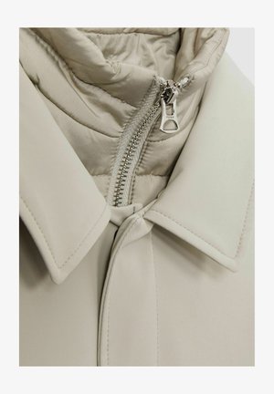 Bež puffer-jope kõrge kaelusega, sileda väliskangaga, tikandiga sisemise voodriga ja hõbedase tõmblukuga.