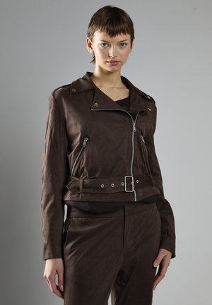 Giubbotto biker in finta pelle scamosciata marrone con zip, vita con cintura e colletto a scatto. Le maniche lunghe e il design aderente creano una silhouette strutturata.