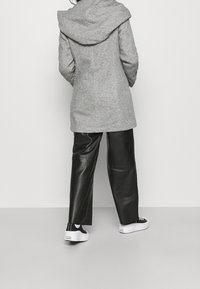 Grå ullblandad kappa med en stor huva, ihopparad med svarta läderbyxor och vita platåskor. Slät textur, enkel design.