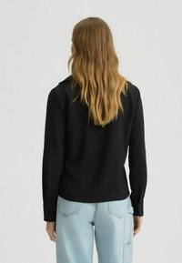 Zwarte langemouwen shirt met een strak design, voorzien van een kraag en knoopmanchetten, gecombineerd met lichtblauwe spijkerbroek.