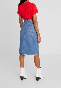 Camiseta roja de manga corta combinada con una falda midi de mezclilla azul claro. La falda presenta un dobladillo sin terminar y dos bolsillos traseros. Botines blancos completan el look.
