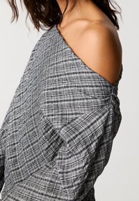 Haut gris à carreaux, épaules dénudées, en tissu texturé, coupe ample avec détails froncés aux épaules.