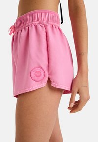 Rosa Boardshorts mit einem elastischen Bund, Kordelzug, seitlichen Schlitzen und einem runden Logo-Patch am Saum. Glatte Stofftextur.