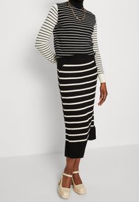 Gestreifter, ribbeliger Pullover in Schwarz-Weiß mit langen Ärmeln, kombiniert mit einem passenden gestreiften Midikleid. Verfügt über einen seitlichen Schlitz und eine strukturierte Oberfläche.