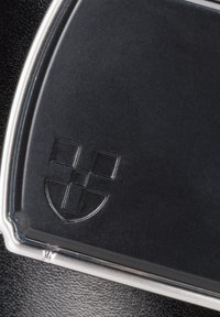 Czarny skórzany produkt o błyszczącej powierzchni, z wytłoczonym logo w rogu i elegancką srebrną krawędzią.