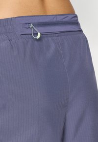 Pantalones cortos morados con un diseño texturizado y acanalado, con una cinturilla elástica. Incluyen un bolsillo con cremallera y un cordón.