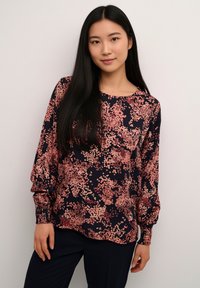 Blouse à manches longues en bleu marine foncé avec motif floral rose, dotée de poignets élastiques et d'un col rond, confectionnée dans un tissu lisse.