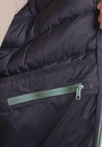 Interior de chaqueta acolchada negra con textura acolchada, que presenta un bolsillo con cremallera de color verde claro y costuras contrastantes a lo largo de las costuras.