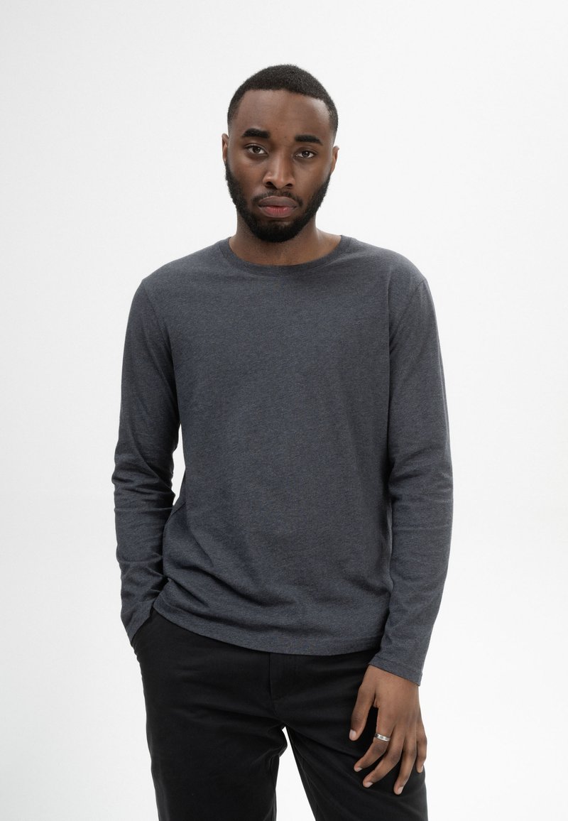 Langärmliges, Rundhalsausschnitt-Shirt aus einem dunklen grauen Stoff mit glatter Textur, kombiniert mit schwarzen Hosen. Minimalistisches Design, keine sichtbaren Muster.