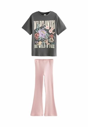 Sötét szürke póló virágos grafikával és a "WILDFLOWERS BE WILD & FREE" felirattal; világos rózsaszín, fodros nadrággal párosítva, amely bordázott anyagból készült.
