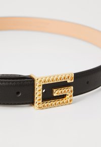 Curea din piele neagră cu o cataramă accentuată cu lanț auriu. Catarama are o formă rectangulară, iar cureaua dispune de mai multe găuri pentru ajustare.