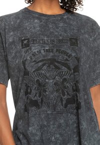  camiseta gráfica de tela gris oscuro con efecto lavado ácido. Presenta un estampado negro con motivos tropicales y el texto "Authentic Roxy Palm Tree People."
