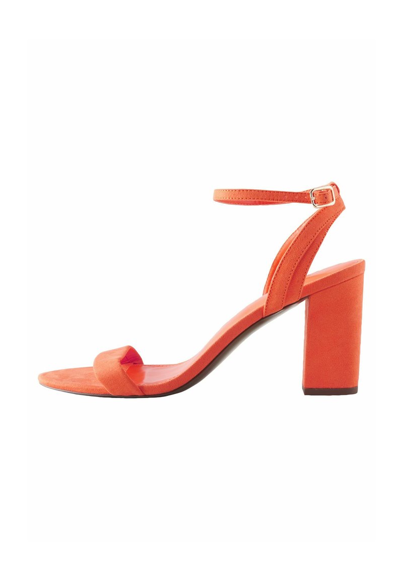 Orange mocka klacksandaler med öppen tå-design, justerbart ankelsnöre och blockklack för stabilitet. Slät textur och elegant silhuett.