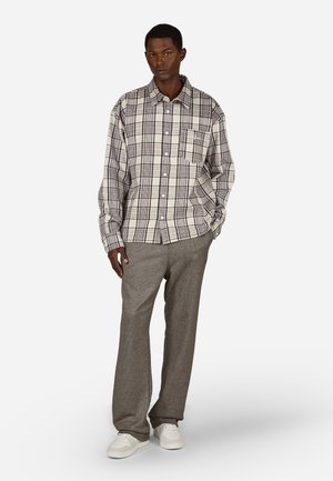 Checked long-sleeve shirt in beige and dark brown, featuring a chest pocket and button closure, paired with gray wide-leg trousers and white sneakers.