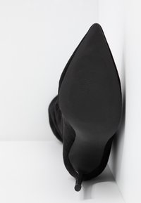 Stivale nero con tacco alto, caratterizzato da una punta affilata e una texture in suede morbido. Presenta un tacco stiletto sottile e una suola piatta e liscia.