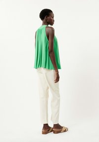 Groene mouwloze top met een geraffineerde achterkant, gecombineerd met lichte witte broeken en tan instapsandalen met een houten hak.