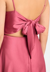 Satin-Kleid in tiefem Pink mit zarten Spaghetti-Trägern und einer großen Schleife hinten, mit einem Cut-out-Bereich und glatter Textur.