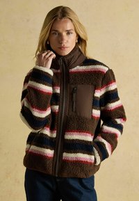 Gestreifte braune und cremefarbene Fleecejacke mit hohem Kragen, ausgestattet mit einer mit Reißverschluss versehenen Brusttasche und einer weichen, strukturierten Oberfläche.