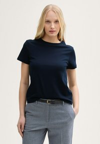 T-shirt a maniche corte blu navy realizzato in tessuto liscio, con un semplice colletto rotondo. Abbinato a pantaloni grigi su misura e una cintura nera.