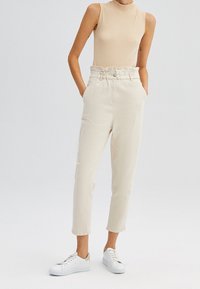 Beiga högmidjade byxor med en samlad midjeband, sidofickor, avsmalnande ben, och parat med vita sneakers. Slätt bomullsmaterial.