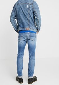 Denimjacka i blekt blått med slitna detaljer. Matchas med jeans i samma blå färg, med smal passform och sömmar på bakfickorna. Svarta stövlar.