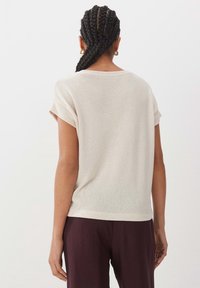 Ljus beige kortärmad topp med uppvikta ärmar, gjord av ett strukturerat stickat tyg. Bärs med mörkt burgundiska byxor, vilket ger en avslappnad silhuett.