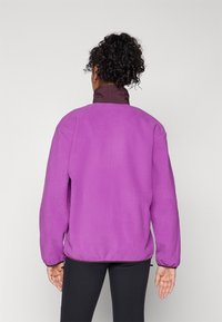 Purple fleece jacket with a high collar and elastic cuffs. Features a relaxed fit and a smooth texture, suitable for casual wear.
