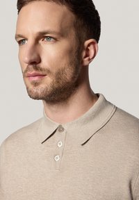 Beżowa koszulka polo z miękkiego materiału, z kołnierzykiem, trzema guzikami oraz subtelnym wzorem teksturowym.
