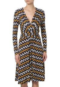 Vestido de manga larga con escote en V profundo y patrón en zigzag en tonos negro, blanco y amarillo; cintura ajustada y falda acampanada.