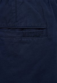 Granatowa tkanina o teksturowanym wykończeniu, z subtelnym wytłoczonym napisem "MUSTANG" na tylnej kieszeni.