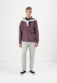 Checkered maroon button-up shirt, light grey sweatpants, and black sneakers. Grey sweater tied around the shoulders. Simple, casual outfit.